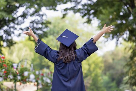 Back view of young woman graduating put her hands up and celebrating feeling so happy.の写真素材