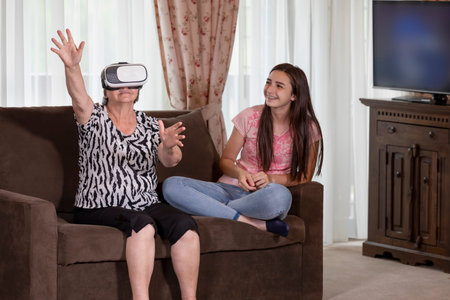 Senior woman with virtual reality headset or 3d glasses having fun with her granddaughter. People...
