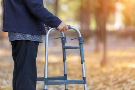 Woman with walker walking in autumn park closeup. Focus on her hand.の写真素材