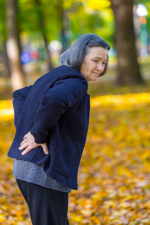Senior woman suffering from backache outdoors in autumn park.の写真素材