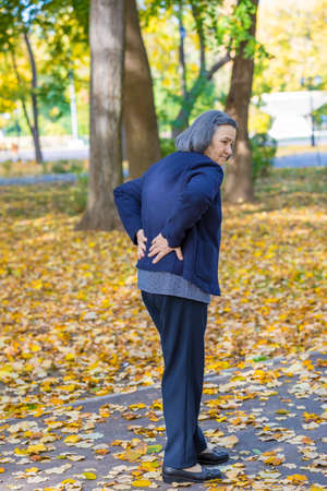 Senior woman suffering from backache outdoors in autumn park.の写真素材