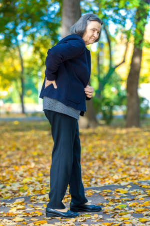 Senior woman suffering from backache outdoors in autumn park.の写真素材