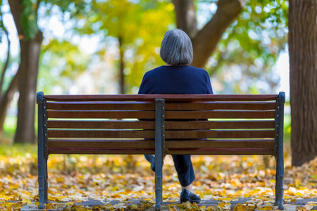 Aged woman sitting on bench in autumn park.の写真素材