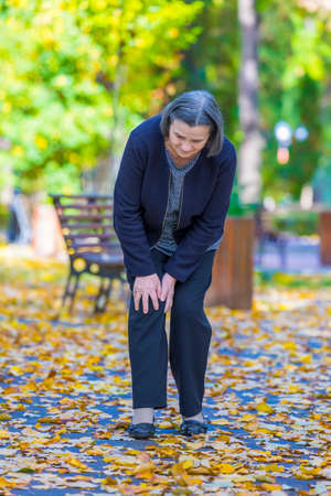 Senior woman having knee pain walking in parkの写真素材