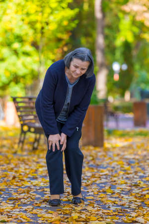 Senior woman having knee pain walking in parkの写真素材