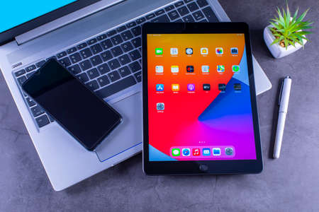 Galati, Romania, March 31, 2021: - Apple release new iPad 8th generation with the powerful A12Â BionicÂ chip, support for AppleÂ Pencil and the SmartÂ Keyboard. iPad 8th generation with smartphone over silver laptop on desktop.のeditorial素材