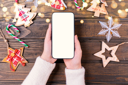 Close up woman holding phone with empty white screen mockup near decorated festive tree, celebrating Christmas, customer shopping online, purchasing gifts, browsing gadget appsの写真素材