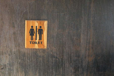 Toilet sign in wood frame on black painted metal wall. Some rusty and scratch on surface of wall.の写真素材