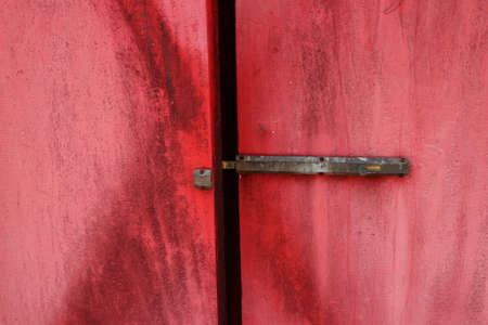 A dark and rusty door lock made from brass in ancient style on painted red wooden door, Thailand.の写真素材