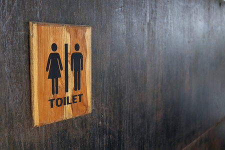 Toilet sign in wood frame on black painted metal wall. Some rusty and scratch on surface of wall.