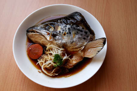 Boiled salmon head with soy sauce (Salmon kabutoni) on white round dish and brown wood background.の写真素材
