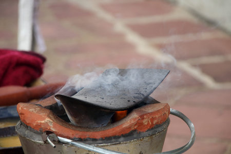 Clay fire pot with iron plow plate is on, smoke over plow and blur brick background, smoke above...