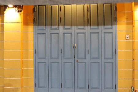Old style gray painted wood doors are closed and light from lamp, color of wall beside the door is...