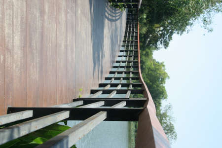 Brown wood bridge and black painted metal fence beside pond in park, Thailand.の写真素材