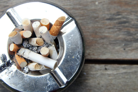 Top view of round shape stainless ashtray on wood plank and tobacco with ash in ashtray.