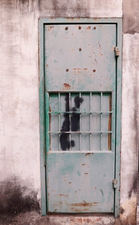 Pale and rusty of green painted metal door and concrete wall, closed rear door of house. Dirty stain on door and cement wall, Thailand.の写真素材