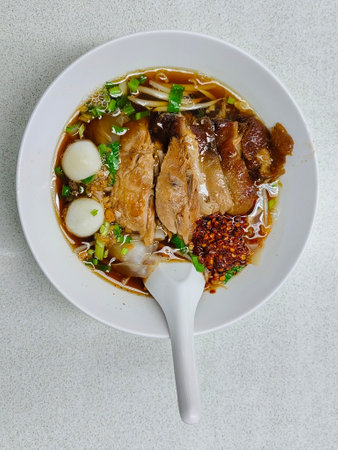 Top view of Five spice braised pork noodle in white bowl with white spoon in bowl on white table.の写真素材
