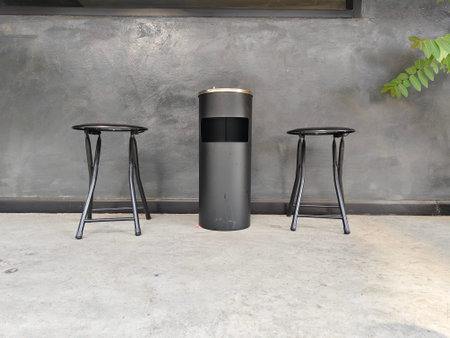 Black painted stainless cylinder bin between black chairs on cement floor and smooth surface...