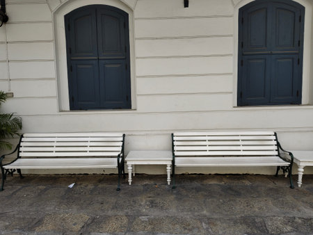 White benchs on concrete floor and white wall with closed windows of building in retro style in Thailand.の写真素材