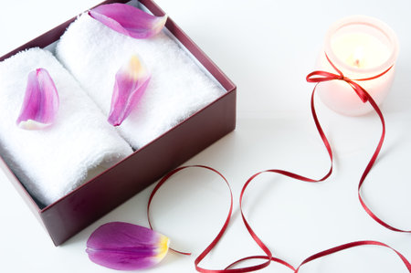 white towels in a box, candle, tied with a ribbon and the petals on a white backgroundの写真素材