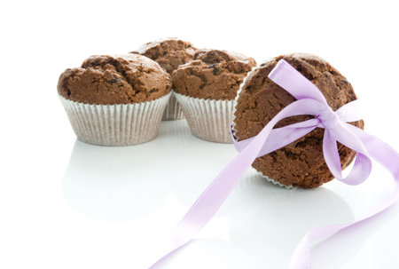 Four chocolate muffins on a white ground, one tied with a purple bowの写真素材