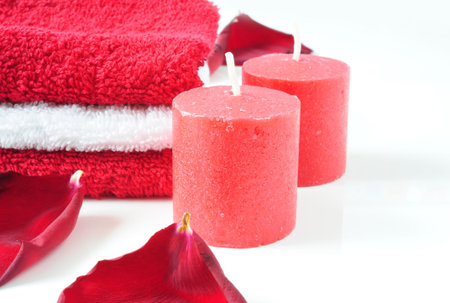 A tower of white and red towels, rose petals and red candles on a white backgroundの写真素材
