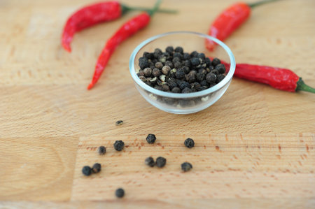 Black pepper in a bowl with a red chili pepper on a wooden table