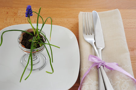 White plate, cutlery, tied with a ribbon on a linen napkin and a flower in the egg shell on a wooden...