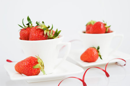 Strawberries in two tea cups with a red ribbon on white backgroundの写真素材