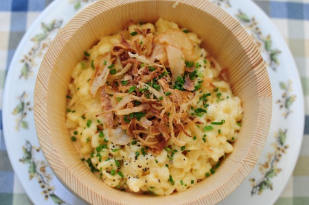 cheese spaetzle with fried onions in a wooden bowl on blue clothの写真素材