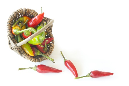 Wicker basket full of colored peppers hot lies on its side on a white background, the three pepper droppedの写真素材