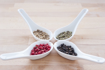 four kinds of peppercorns with white porcelain condiment spoons on a wooden tableの写真素材