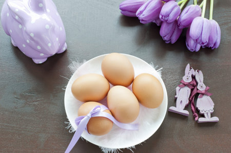 five eggs on a white porcelain plate with pink feathers, a pair of wooden bunnies, ceramic rabbit...