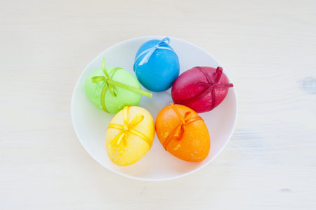 Five colored eggs, tied with satin ribbons, on a white porcelain plate, on wooden table