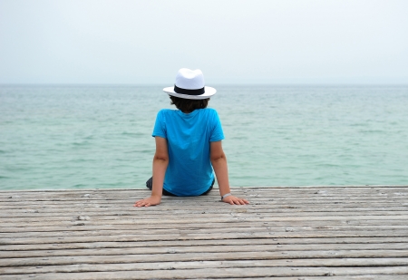 boy of school age in the hat on the pier watching the waterの写真素材