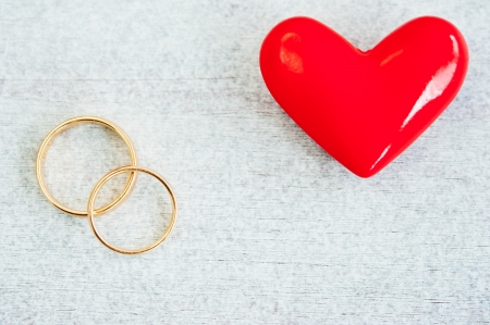 two old, scratched wedding rings on the wooden table next to a red heartの写真素材