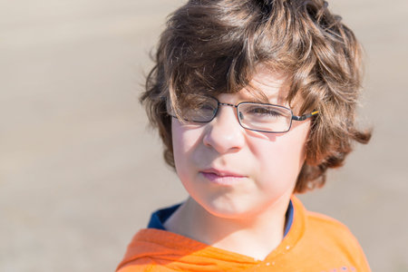 European school-age boy with glasses, with brown hair on the background of a sandy beach in an...