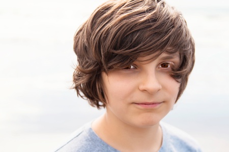 European school-age boy on a background of sand, brown hair ruffled by the wind, close-upの写真素材