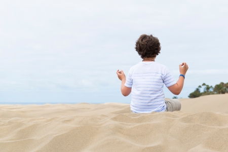 European school-age boy sitting in the lotus position on a sandy duneの写真素材
