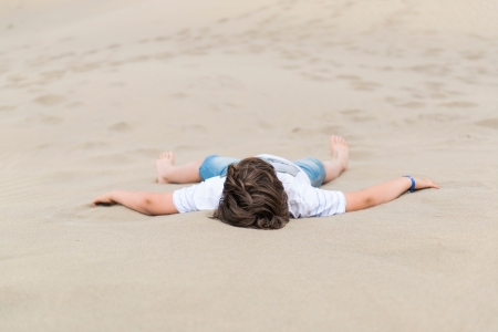 European boy is lying on the white sand in clothes outstretched handsの写真素材