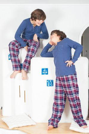 Two European boy in pajamas, one sits on top of the second is downstairs, looking at each otherの写真素材