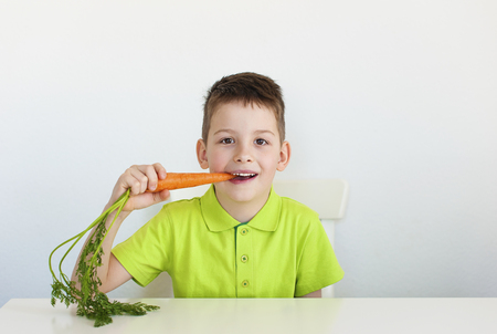 one young brunette boy eating carrot. white blackground.の写真素材
