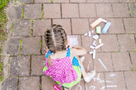 Girl in a colorful dress sits on concrete asphalt square road. Child drawings paintings on asphalt concrete.の写真素材