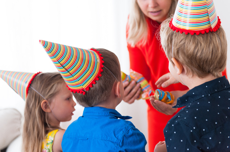 Two boys and one girl in party hats turned away from the camera take bright confetti from moms handの写真素材