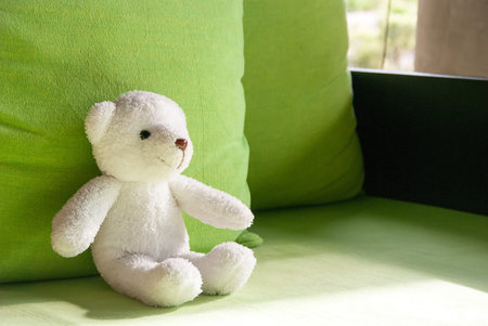 Smilely white teddy bear sit on sofa and lay on green pillowの写真素材