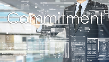 the businessman in the office is writing on the transparent board: Commitmentの写真素材