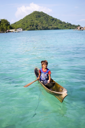 MABUL ISLAND, SABAH, MALAYSIA - MARCH 3: local sea gypsy kid paddles a boat March 3, 2013 in Mabul Island, Sabah, Malaysia. Children live here do not attend school for lack of means and resourcesのeditorial素材