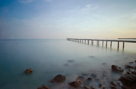 Broken wood bridge and waves crashing on sea at during sunsetの写真素材