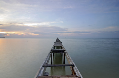 Broken wood bridge and waves crashing on sea at during sunsetの写真素材