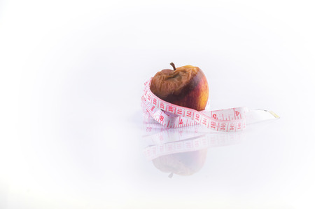 Wilted rotten apple and measuring tape on white background. Diet conceptの写真素材